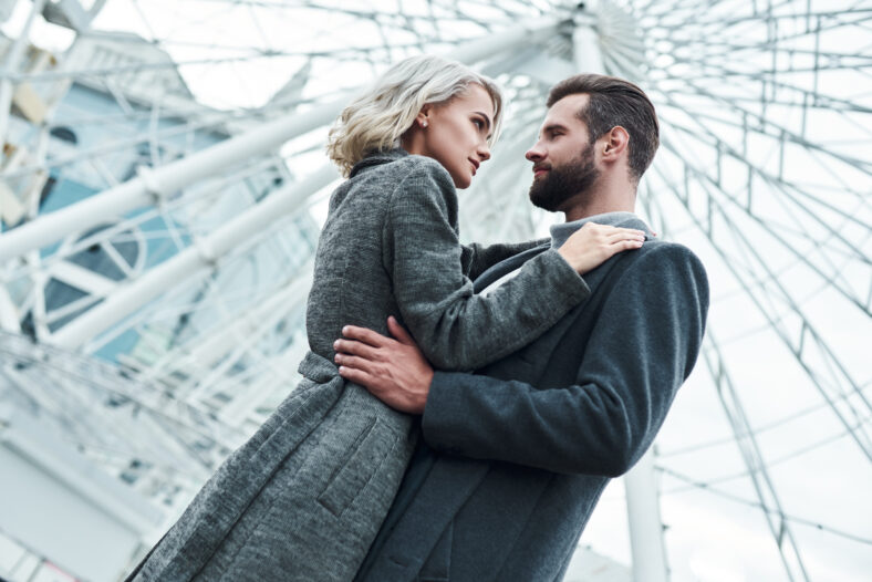 Romantic date outdoors. Young couple standing at entertainment park hugging looking at each other passionate bottom view close-up