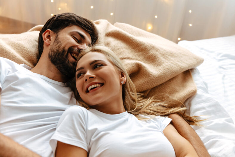 Love. Fun. Emotions. Young couple are laughing while lying together on the bed