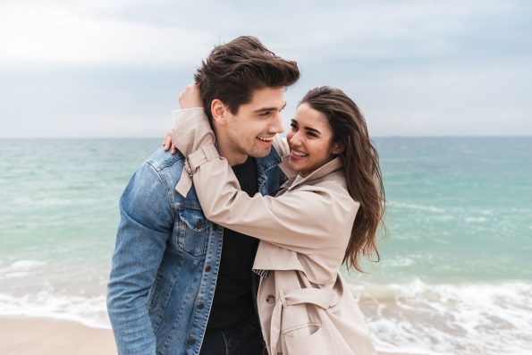 Happy young couple in love wearing autumn coats spending time together at the seaside, hugging