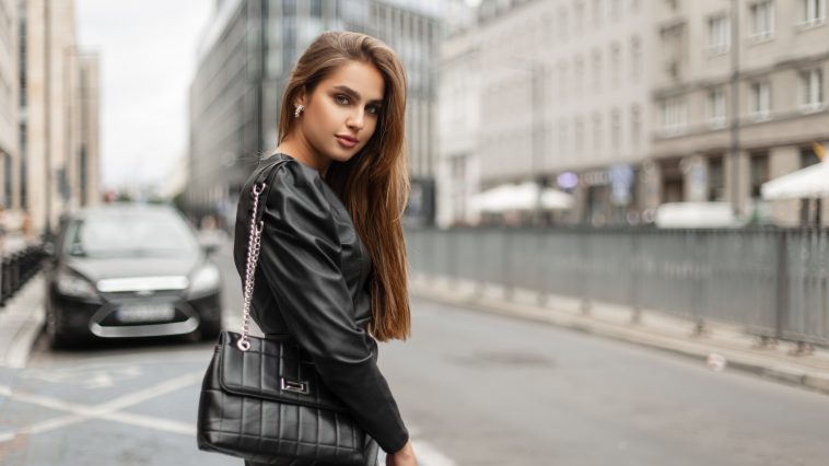 Elegance fashion pretty woman in stylish black dress with leather fashionable bag walks in modern city. Business beauty lady