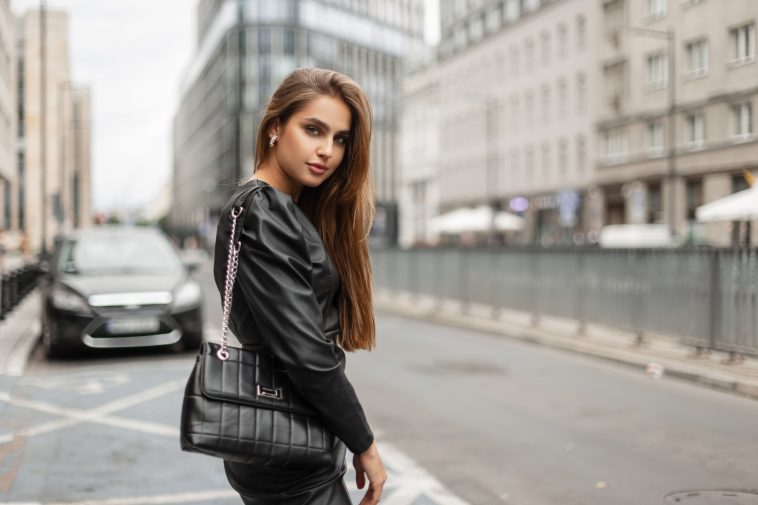 Elegance fashion pretty woman in stylish black dress with leather fashionable bag walks in modern city. Business beauty lady