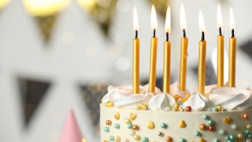 Beautiful birthday cake with burning candles on blurred background, closeup. Space for text