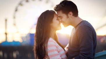 romantic couple in front of santa monica amusement park at sunset.