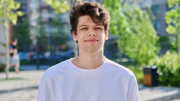 Headshot portrait of smiling, handsome student guy 19, 20 years old, looking at camera outdoors. Youth, urban style, young man, lifestyle concept