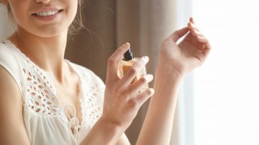 Beautiful young woman with bottle of perfume at home, closeup