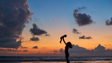 silhouette of mother carrying child in front of beautiful ocean beach sunset