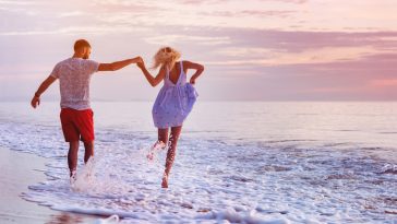 Happy couple runs in wave splashes at romantic sea sunset