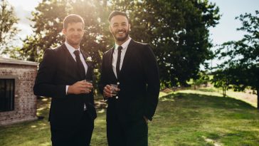 Portrait of handsome young groom standing with his friend having drinks at wedding party. Bridegroom and best men after wedding ceremony having drinks at park.