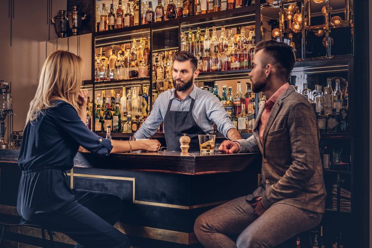 Stylish brutal bartender serves an attractive couple who spend an evening on a date.