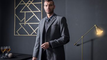 Portrait of stylish handsome business man in luxury apartment. Businessman in dark interior. man in fashionable business gray suit in house. wine on table and night lamp in house of rich man