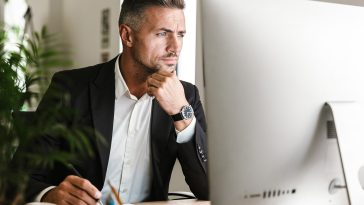 Image of confident businessman 30s wearing suit working in office and looking on computer