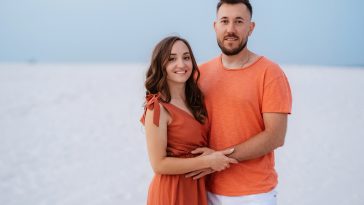 young couple in orange clothes with dog in the desert white sands