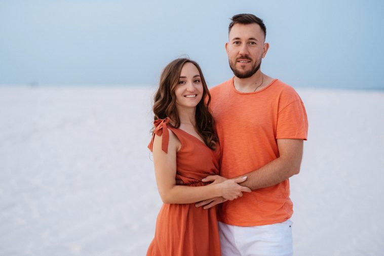 young couple in orange clothes with dog in the desert white sands