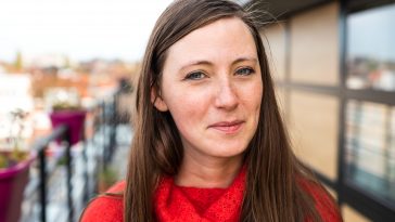 Portrait of an attractive thirty year old white woman in red posing on a terrace against a contemporary apartment, Brussels