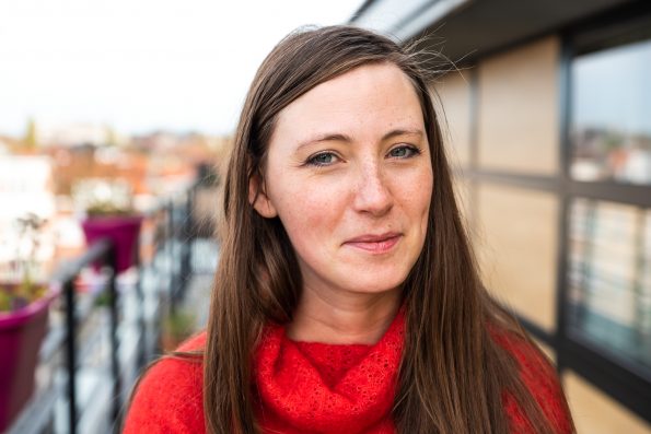 Portrait of an attractive thirty year old white woman in red posing on a terrace against a contemporary apartment, Brussels