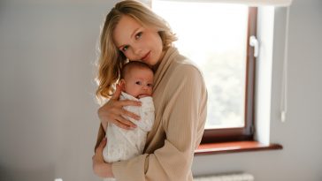 White young woman in housecoat holding her newborn baby in bedroom