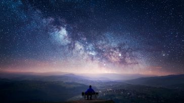 A man sitting on a bench staring at a starry sky with a Milky Way