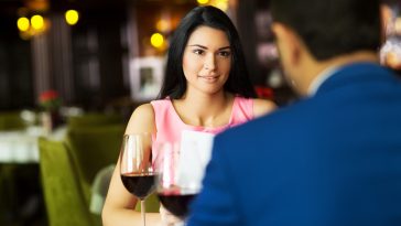 Beautiful young couple with glasses of red wine in luxury restaurant.Focus on girl