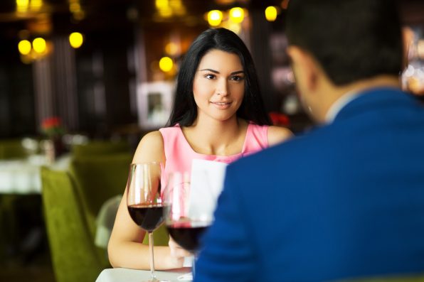 Beautiful young couple with glasses of red wine in luxury restaurant.Focus on girl