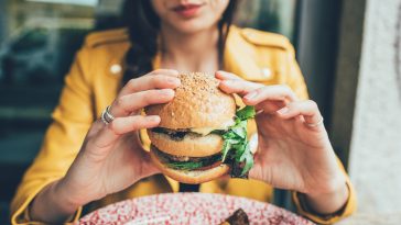 Close up on the hands of a young woman sitting holding an hamburger - hunger, food, meal concept