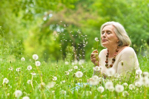 Portrait of a beautiful senior woman in green field with dandelions