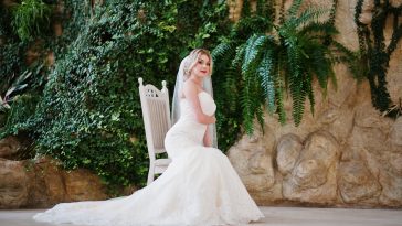 Gorgeous blonde bride sitting on chair and posed at great awesome wedding hall