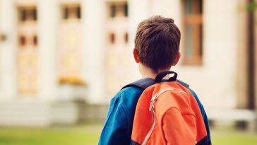 Boy with rucksack infront of a school building. Child with a backpack