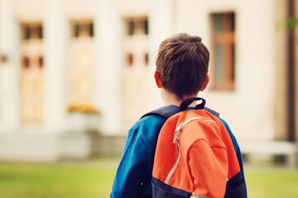 Boy with rucksack infront of a school building. Child with a backpack