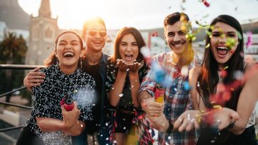 Group of friends enjoying party and throwing confetti. Friends having fun at rooftop party.