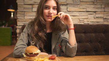 young lovely woman sitting in cafe with burger and chips, eating french fries