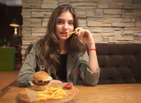 young lovely woman sitting in cafe with burger and chips, eating french fries