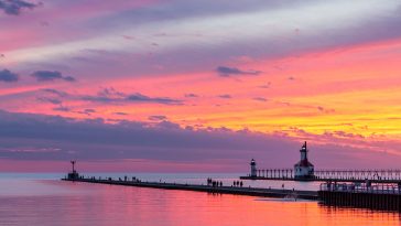 The setting sun paints the sky above Lake Michigan in glorious color and silhouettes the lighthouses and sightseers on the North and South Pier at St. Joseph, Michigan.