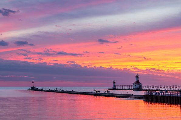 The setting sun paints the sky above Lake Michigan in glorious color and silhouettes the lighthouses and sightseers on the North and South Pier at St. Joseph, Michigan.