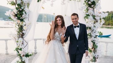 Happy family of groom and bride at wedding day ceremory with arch on background shows their hands with rings. Smiling newlyweds together in wedding suits. Concept of love and happiness.