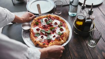 cropped shot of woman carrying plate with delicious pizza margherita to serve on table at restaurant