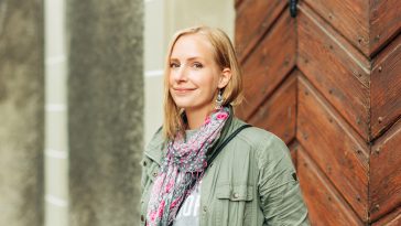 Outdoor portrait of beautiful blond woman, posing outdoors, wearing khaki color parka and pink scarf