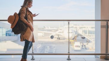 Travel and technology. Pretty young woman using smartphone waiting for boarding in airport terminal.