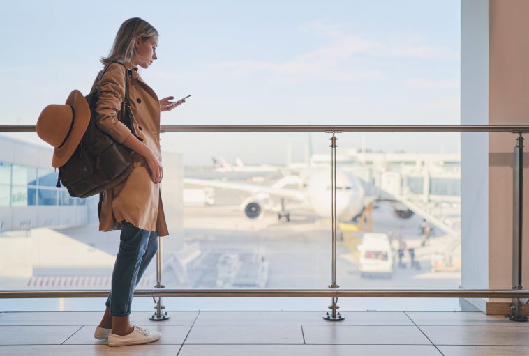 Travel and technology. Pretty young woman using smartphone waiting for boarding in airport terminal.