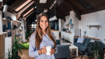 Smiling young woman holding a mug while standing in modern apartment.