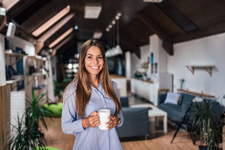 Smiling young woman holding a mug while standing in modern apartment.