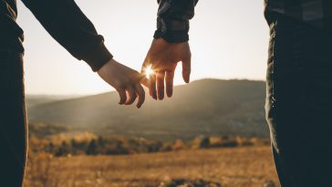 Close up view of holding hands. True love, partnership, love goals. Beautiful romantic moment between two lovers. Hands joining together with sunlight flare in the background.