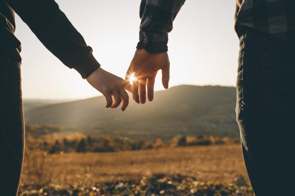 Close up view of holding hands. True love, partnership, love goals. Beautiful romantic moment between two lovers. Hands joining together with sunlight flare in the background.