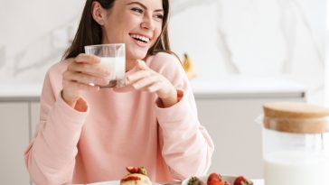 Beautiful smiling young girl having tasty healthy breakfast while sitting at the kitchen table