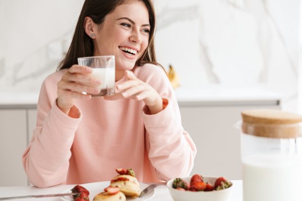 Beautiful smiling young girl having tasty healthy breakfast while sitting at the kitchen table