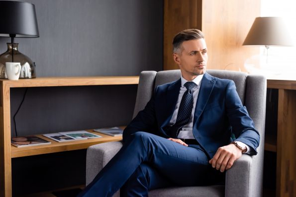 handsome businessman in suit sitting in armchair and looking away