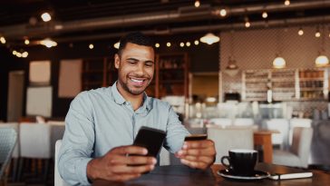 Man using mobile smartphone and credit card for online shopping in coffee shop