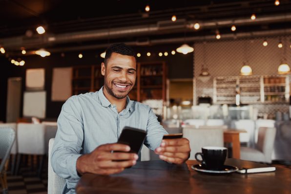 Man using mobile smartphone and credit card for online shopping in coffee shop