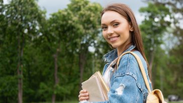 cheerful and attractive student looking at camera and holding books