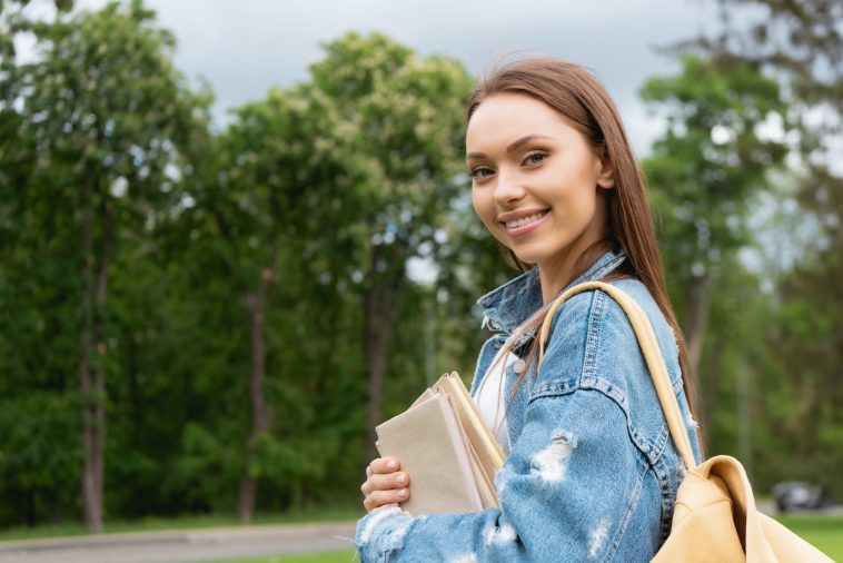 cheerful and attractive student looking at camera and holding books