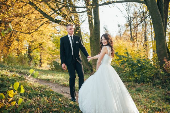 Sunshine portrait of happy bride and groom outdoor in nature location at sunset. Warm summertime. Happy couple with a beautiful bouquet of flowers. Wedding photo. Couple in love. Autumn wedding